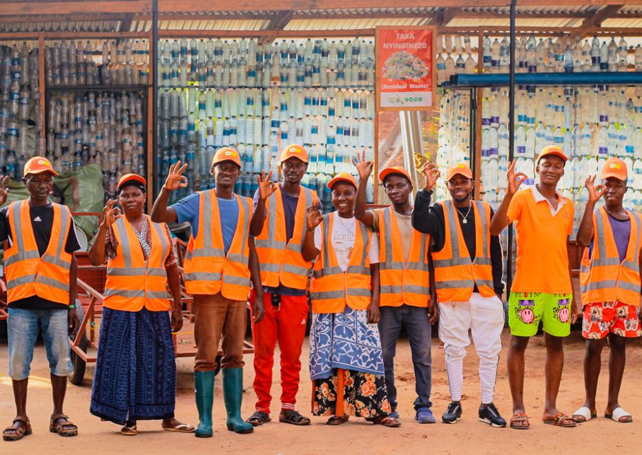 Portrait of a group of waste pickers, wearing orange bests and hats and smiling at camera