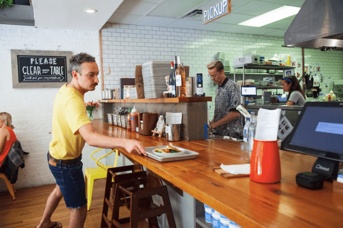 Man wearing a yellow shirt picking up a tray of food at a cafe's counter