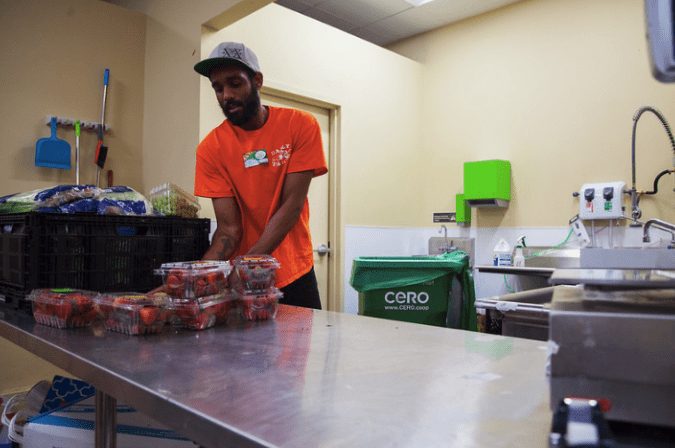 Man wearing orange shirt unpacking some strawberries on a metallic table, commercial kitchen