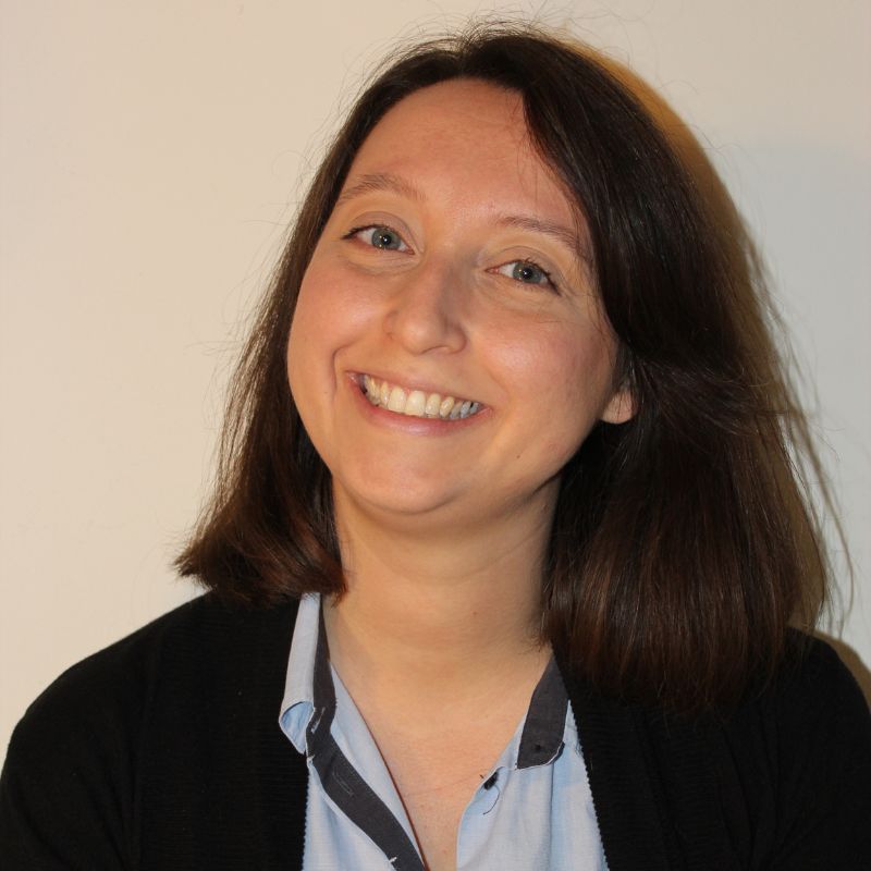 Headshot of white woman smiling at the camera. She's wearing a dark cardigan and a light-colored shirt.