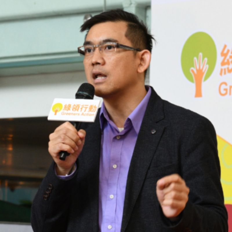 portrait of asian man holding a microphone and giving a speech. He's wearing a dark blazer and a llight purple shirt