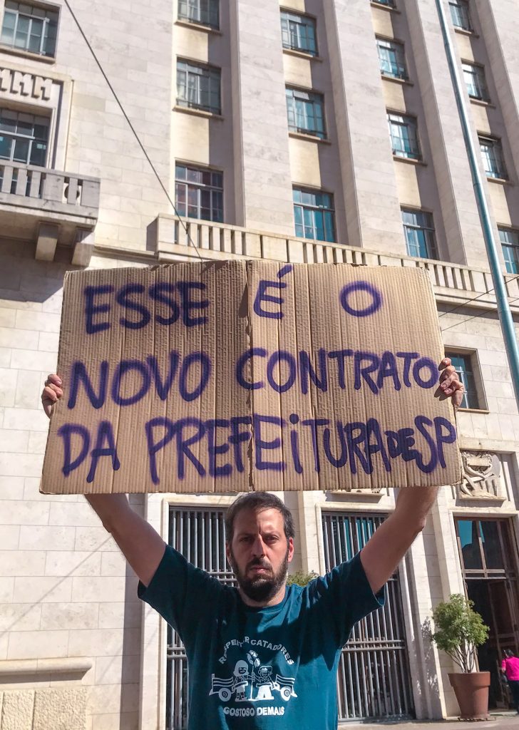 hombre sosteniendo un cartel sobre su cabeza. Al fondo hay un edificio. 
