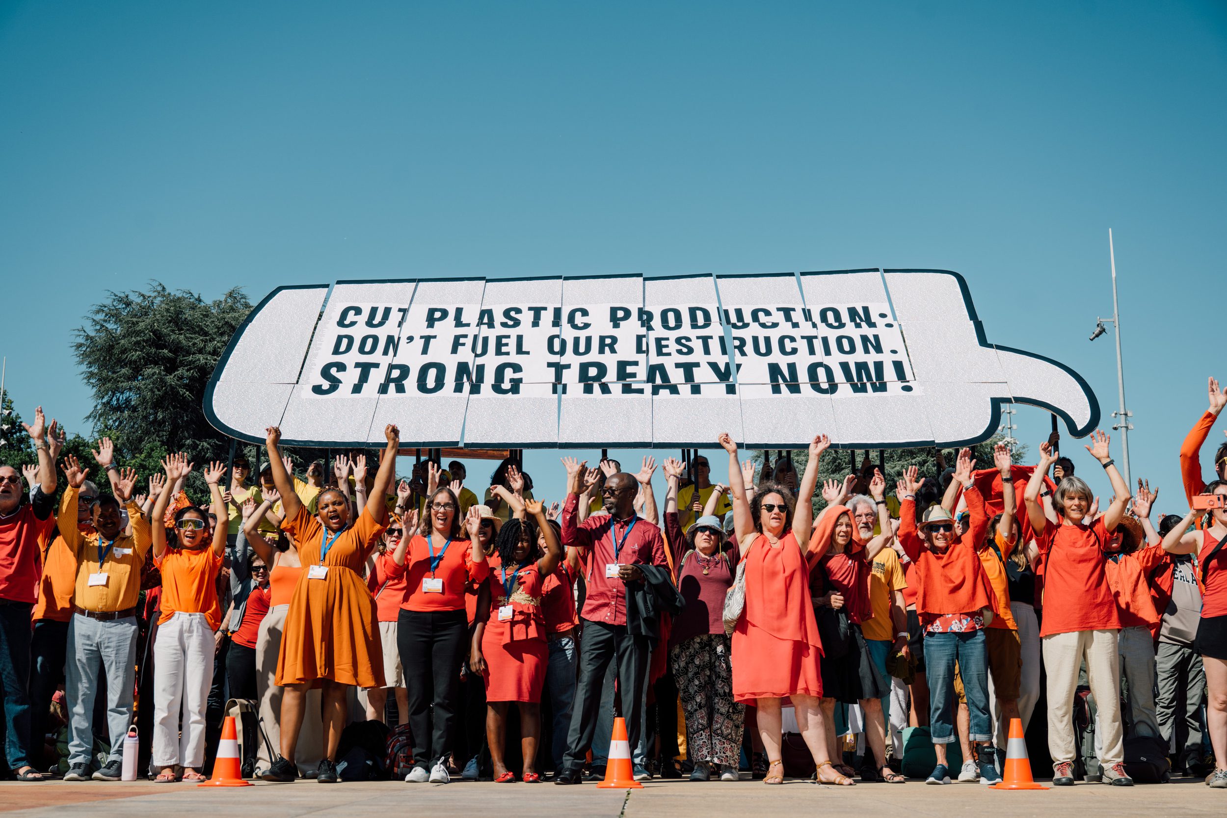 people with orange shirts raising their arms under a sign that reads, 