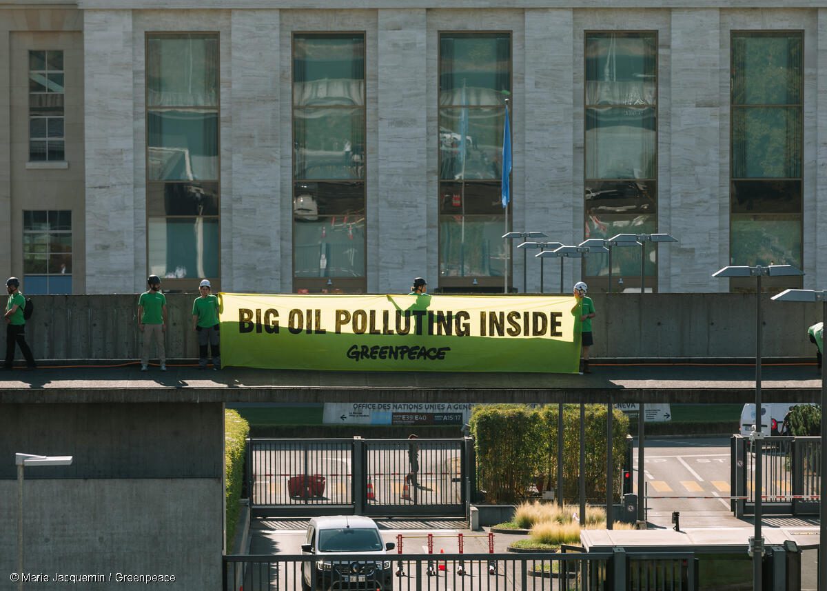 Greenpeace activists paint Geneva streets black to call out Big Oil’s chokehold on Global Plastic Treaty talks, banner text reads Big Oil Polluting Inside